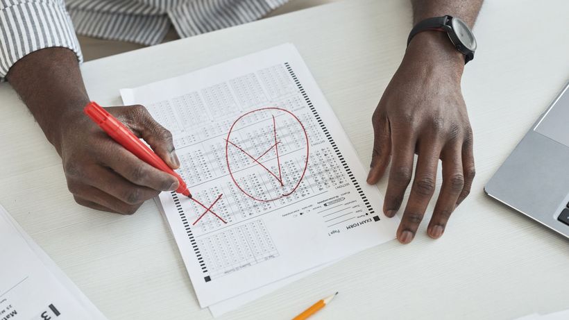 Close-up of a teacher marking a test paper with a red marker on a desk