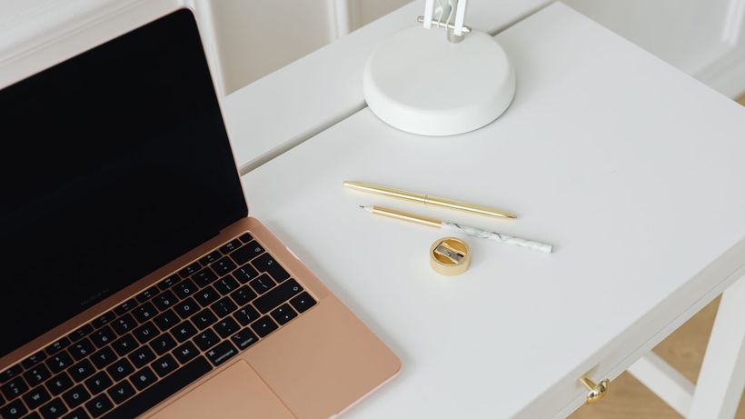 A clean, minimalist desk setup with a laptop, pens, and lamp, perfect for workspaces