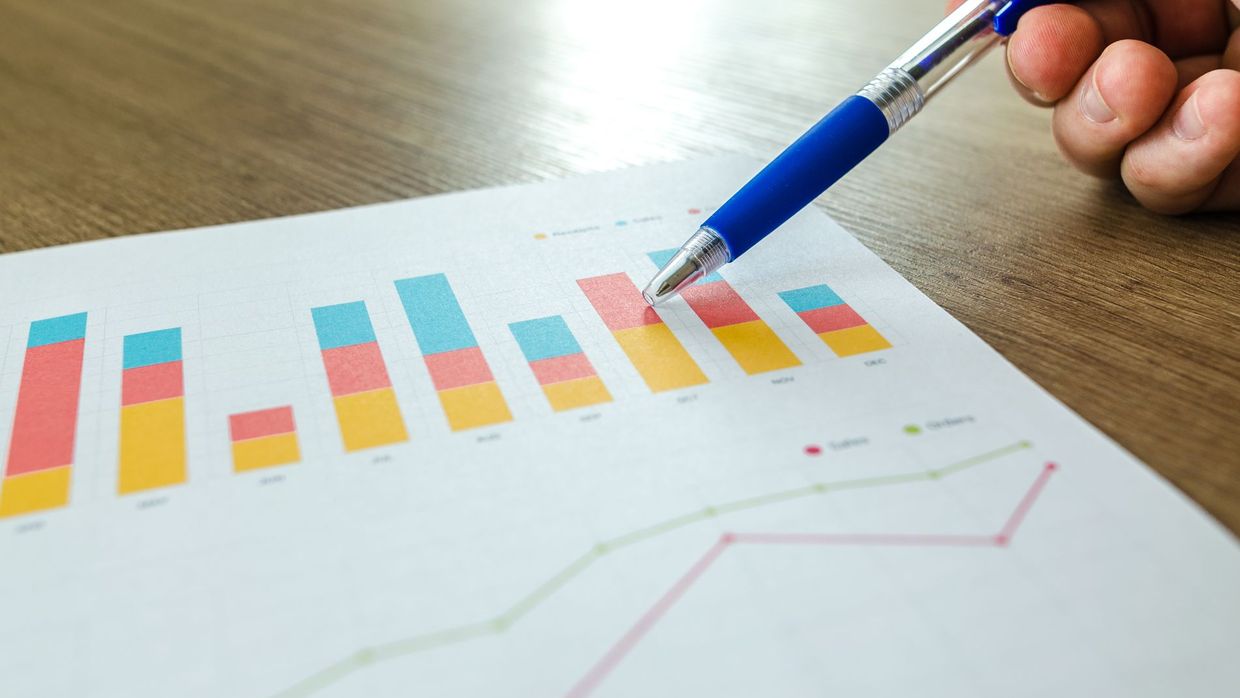SEO job market predictions: detailed close-up of a hand pointing at colorful charts with a blue pen on wooden surface