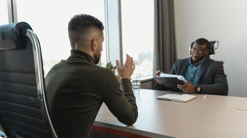 Two men in a job interview setting in a modern office with large windows