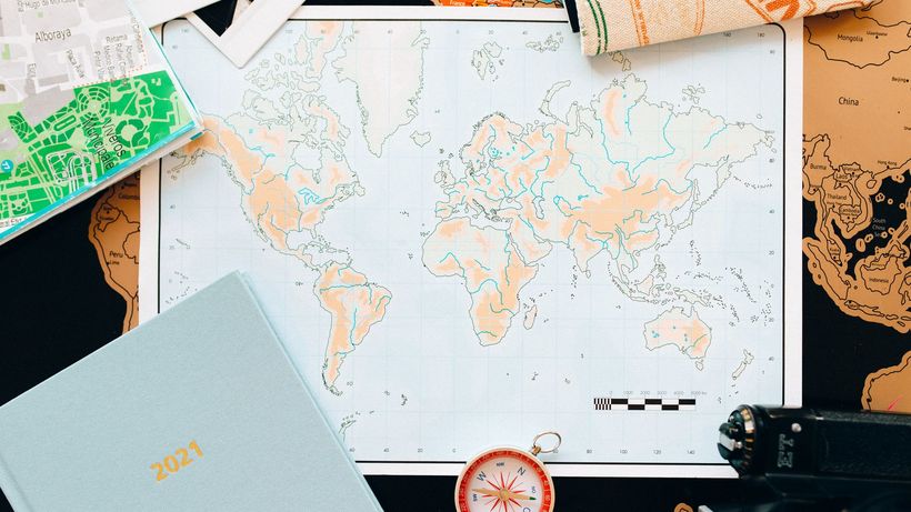 Flat lay of travel essentials including a world map, compass, and planner, perfect for planning your next adventure