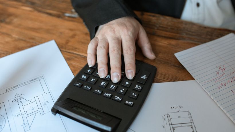 Hand using calculator for architectural calculations on blueprints