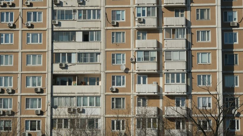 Front view of a sunlit urban apartment building with balconies and air conditioning units