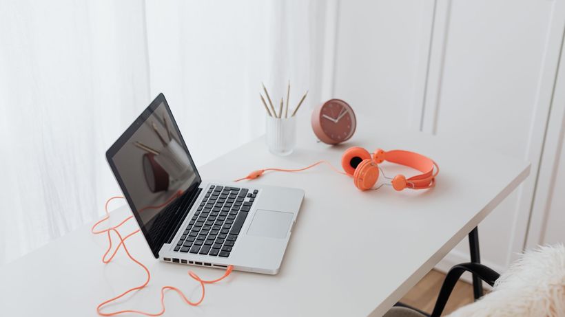 Minimalist workspace featuring a laptop and orange headphones on a clean white desk