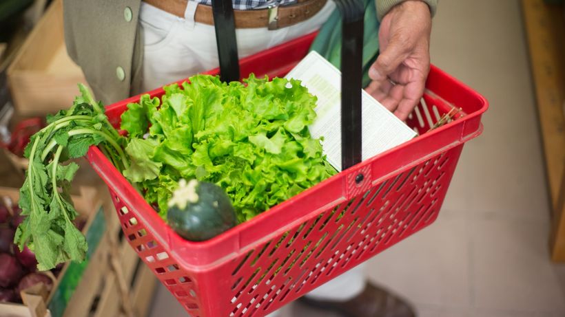 Close-up of a hand carrying a shopping basket filled with fresh greens in a market