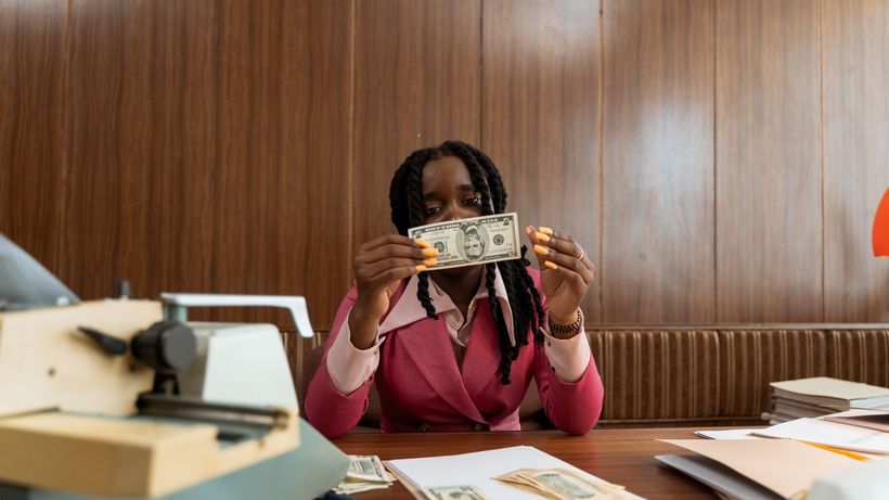 Professional woman at desk examining banknotes, surrounded by documents and coins