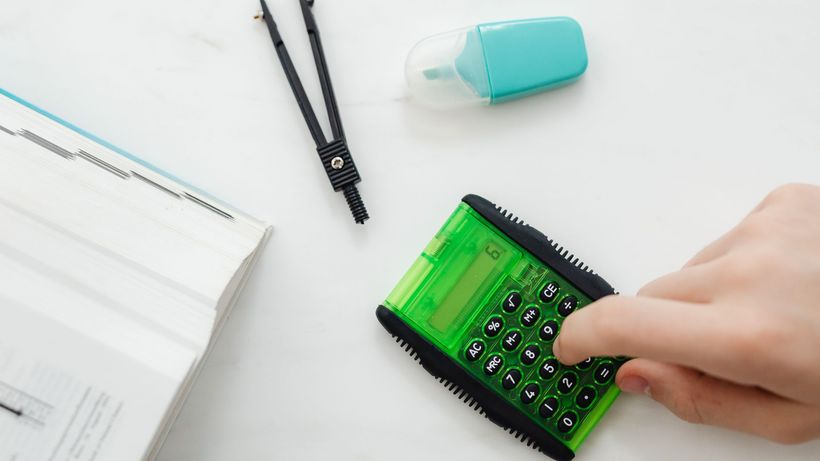 Close-up of a hand using a green calculator with stationery for studies or business calculations
