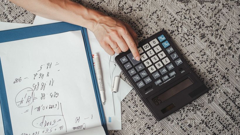 Top view of a hand calculating numbers with a large calculator and notes on a desk