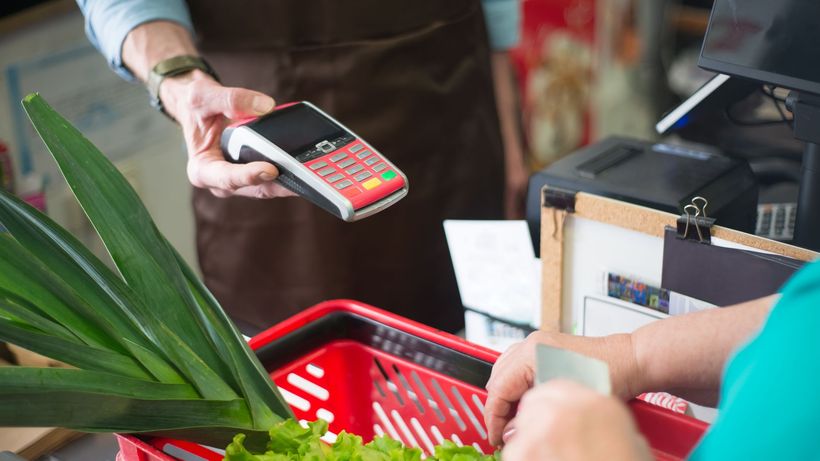 A customer using a contactless payment method at a grocery store checkout with fresh produce