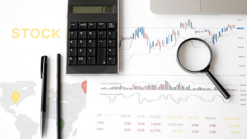 Flat lay of stock market analysis tools including calculator, graphs, and magnifying glass