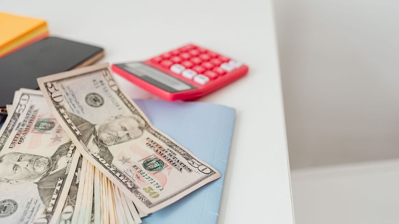 Close-up of notebooks, US dollars, and a calculator on a desk