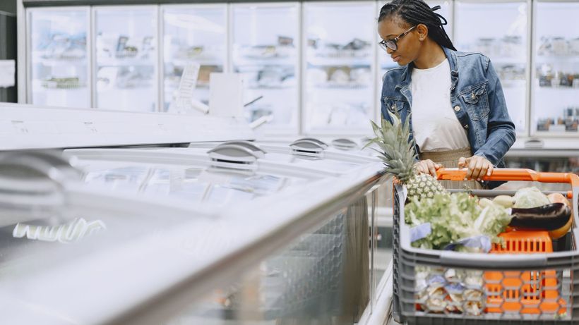 Woman shopping in supermarket with full cart of groceries wearing eyeglasses and denim jacket