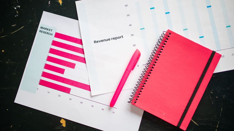 Overhead shot of a desk with charts, a red notebook, and a pen for business analysis