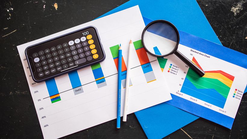 Top view of financial charts with a smartphone calculator, magnifying glass, and pencils on a desk