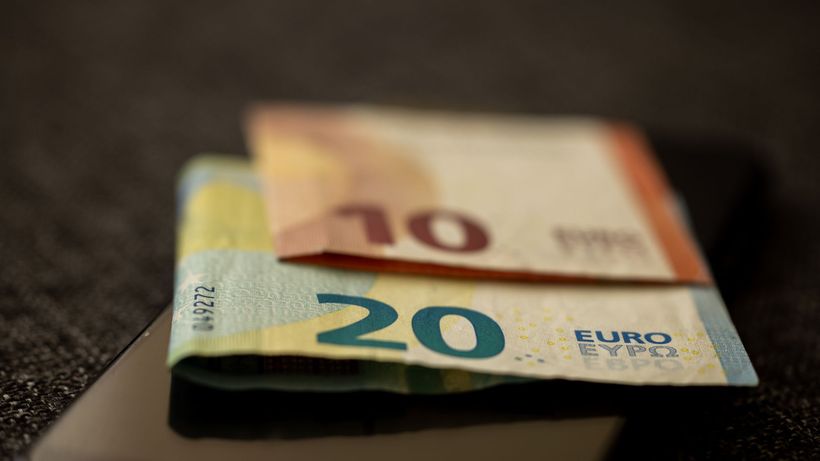 A detailed close-up shot of 10 and 20 euro banknotes placed on a smartphone, representing finance and technology