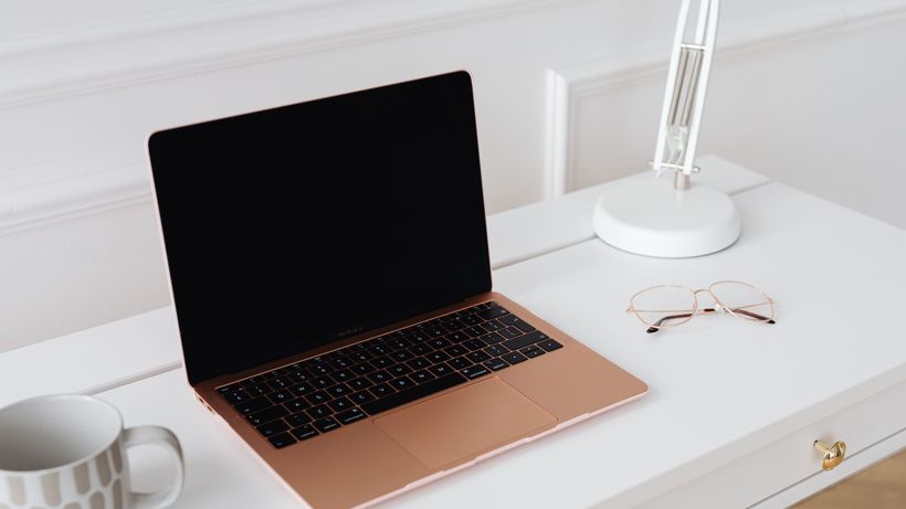 A modern sleek workspace featuring a laptop, desk lamp, and glasses on a white table