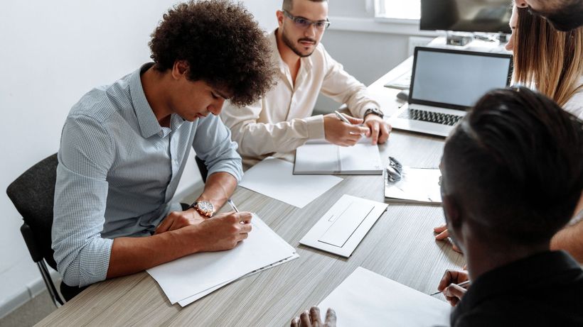 A multi-ethnic group working together at a desk with laptops and papers