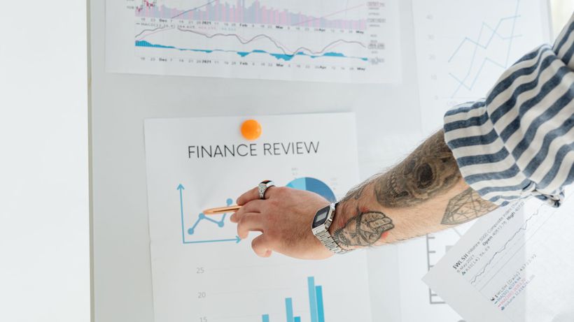 A person with tattooed arms presenting financial data using charts and graphs on a whiteboard