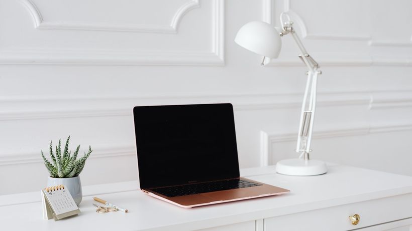 A clean and elegant workspace featuring a laptop, desk lamp, and plant on a white desk