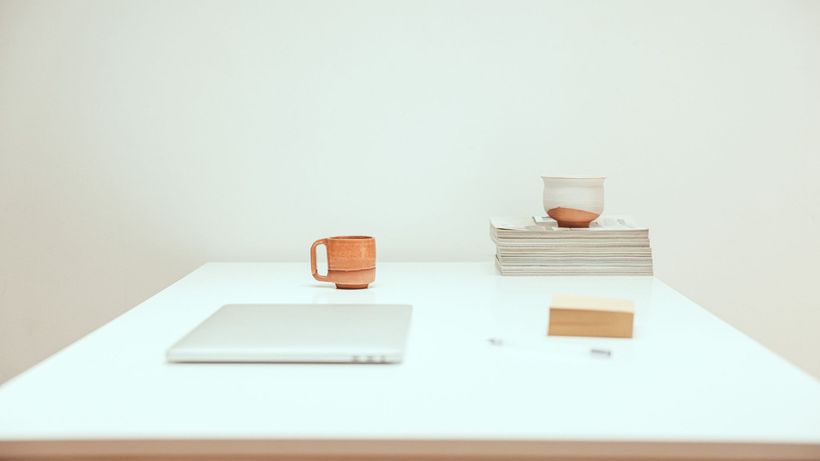 Simple minimalist workspace featuring a laptop, mug, and stacked magazines