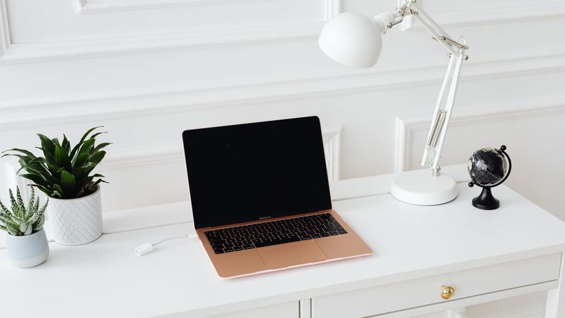 Clean and stylish workspace featuring a laptop, desk lamp, and potted plants on a white desk