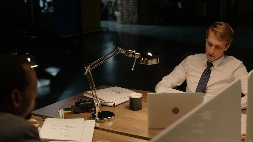 Two professionals working late in an office, reviewing documents under a desk lamp