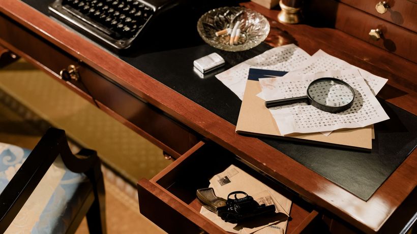 A moody vintage detective's desk with typewriter, magnifying glass, and secret documents