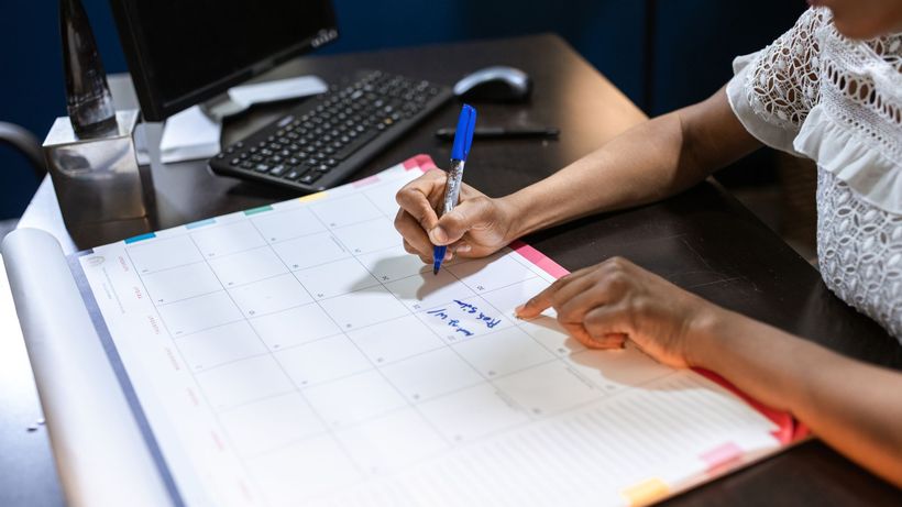 Person writing important notes in a desk calendar with a pen, set in an office