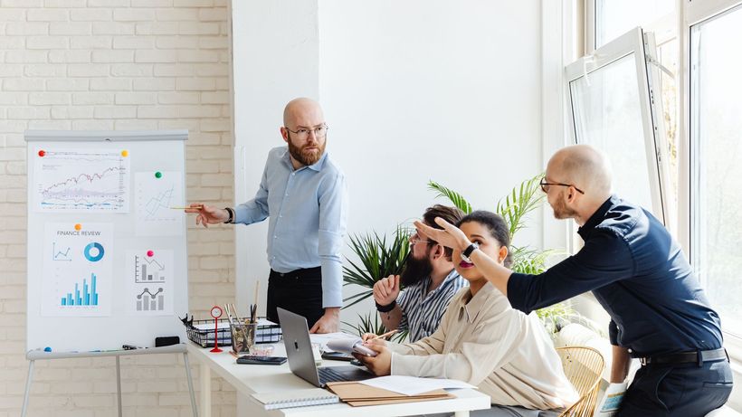 A group of professionals engaged in a business meeting, discussing financial graphs on a whiteboard