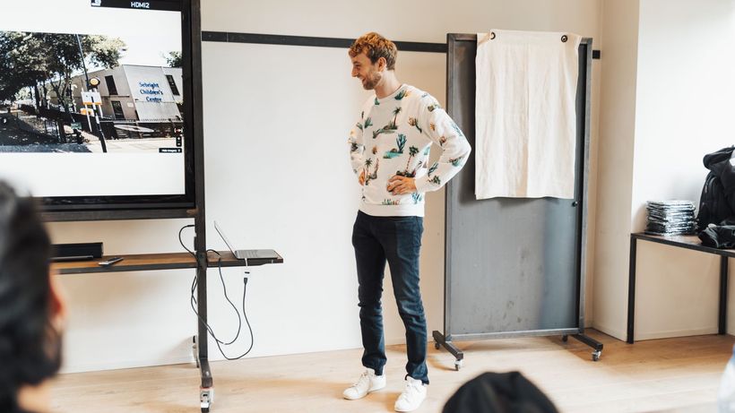 Man presenting on a large screen in a modern office setting, engaging an audience