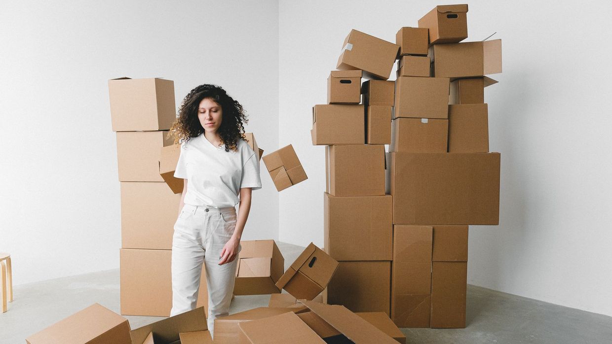 Site migrations: young female with curly hair between piles and flying cardboard containers after moving into house on light