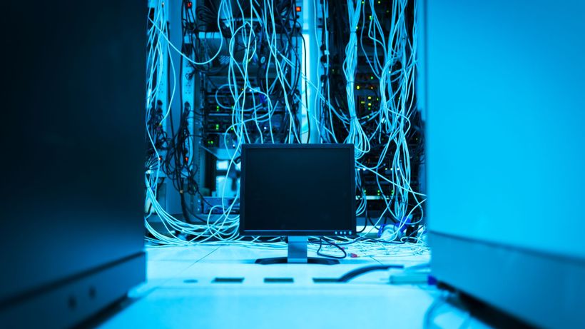 A complex network of cables in a data center with a monitor in the foreground