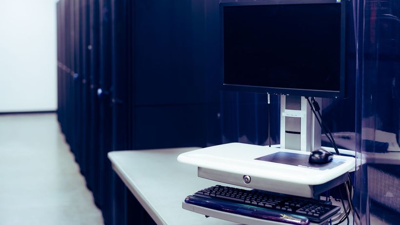 Contemporary computer with black screen placed on stand near row of server steel racks in data center