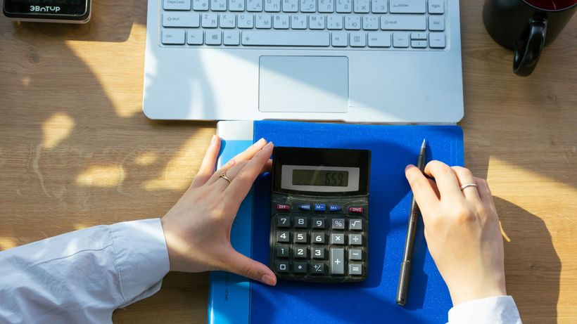 Hands using calculator on a desk with a laptop, pen, and notebook. Perfect for office or finance themes