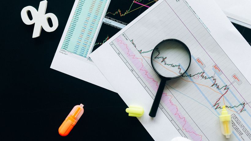 High-angle view of financial charts, showcasing stock market analysis with magnifying glass and highlighters