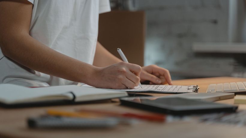 Close-up of individual writing on a clipboard at a desk with office supplies