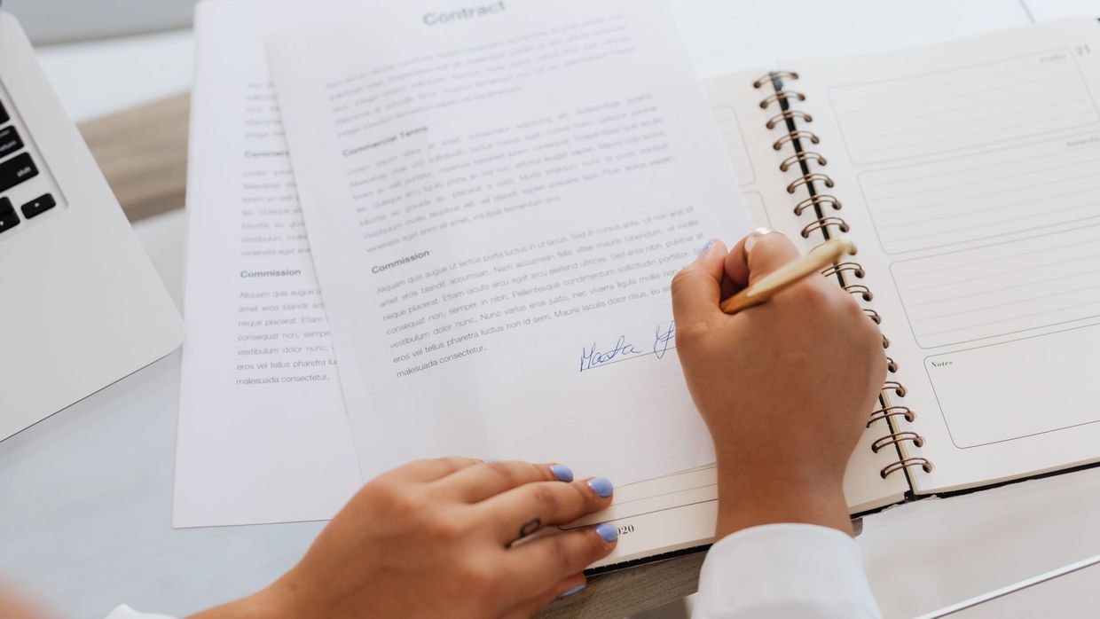 Terms of use: close-up of hands signing a contract on a desk with office supplies, symbolizing legal agreements