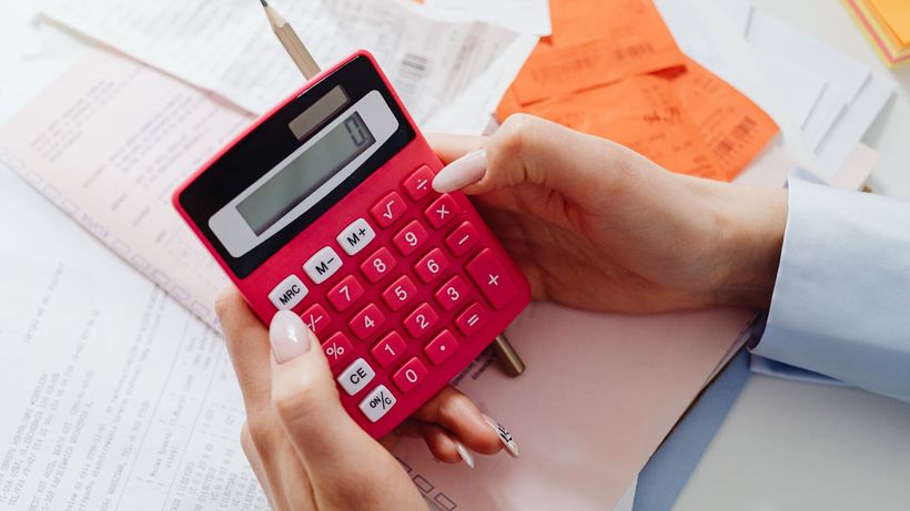 Close-up of hands holding a red calculator, managing finances with documents and receipts