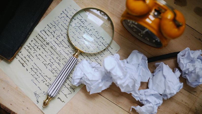 A vintage scene featuring a magnifying glass on a handwritten letter, crumpled papers, and an old clock